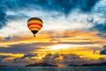 Bunter Heißluftballon schwebt über einem See bei Sonnenuntergang mit dramatischem Wolkenhimmel.