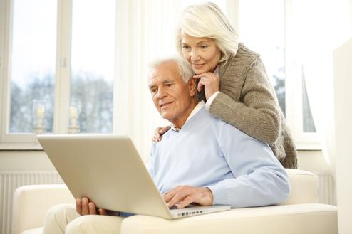 Paar sitzt auf einer Couch und schaut gemeinsam auf einen Laptop in einem hellen Raum.